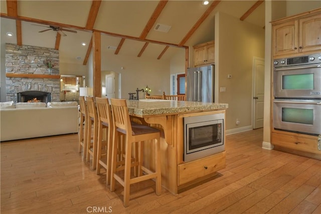 173 Grizzly Rd, Lake Arrowhead, CA 92352 - kitchen featuring appliances with stainless steel finishes, a stone fireplace, a kitchen bar, high vaulted ceiling, and light wood-style floors
