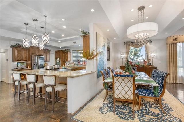 kitchen featuring kitchen peninsula, stainless steel fridge, a tray ceiling, hanging light fixtures, and light stone counters