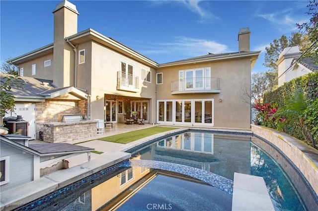 rear view of house with a balcony, a patio area, a pool with hot tub, and exterior kitchen