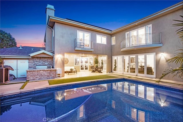 pool at dusk featuring an outdoor kitchen and a patio