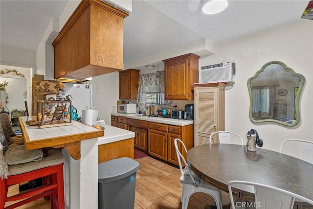 kitchen featuring tile counters, white fridge, light hardwood / wood-style floors, kitchen peninsula, and a wall mounted AC