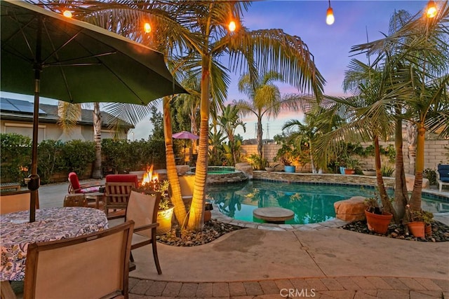 pool at dusk with an in ground hot tub, a patio area, and a fire pit