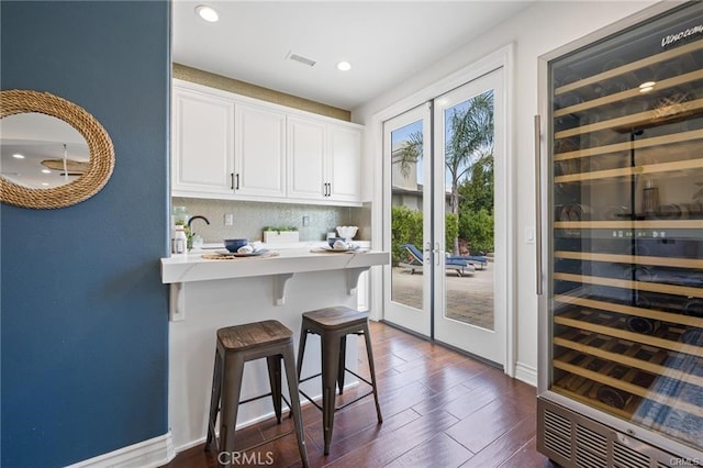 kitchen with white cabinetry, sink, backsplash, a kitchen breakfast bar, and dark wood-type flooring