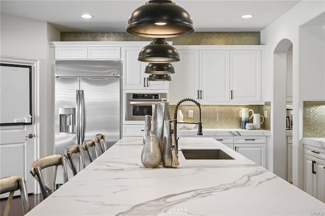 kitchen featuring appliances with stainless steel finishes, white cabinetry, a kitchen breakfast bar, light stone counters, and tasteful backsplash