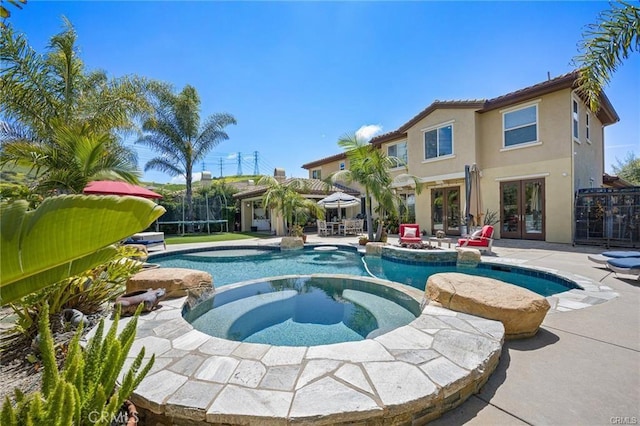 view of swimming pool with an in ground hot tub, a patio, a trampoline, and french doors