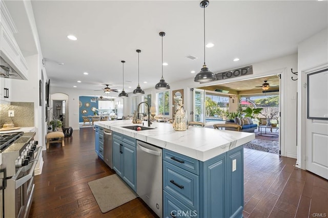 kitchen with sink, a center island with sink, stainless steel appliances, blue cabinets, and decorative light fixtures