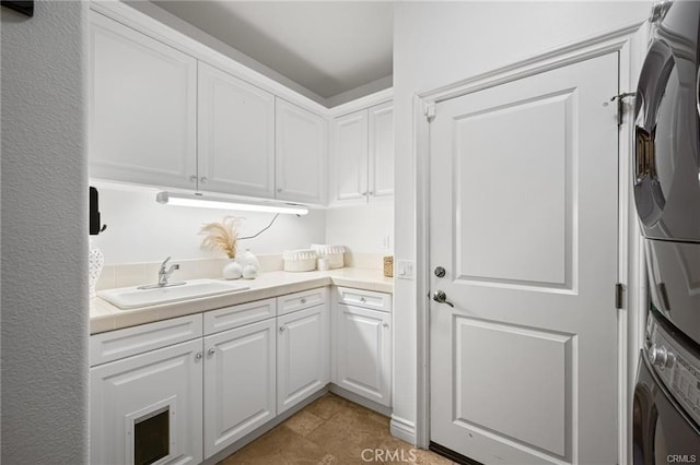 laundry room with sink, light tile patterned floors, cabinets, and stacked washer and clothes dryer