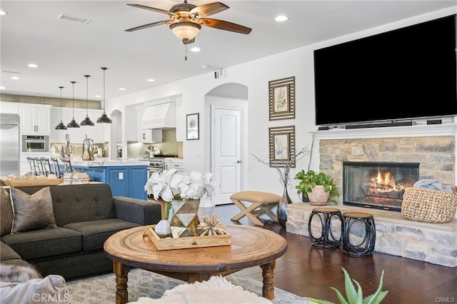 living room with dark wood-type flooring, ceiling fan, a fireplace, and sink