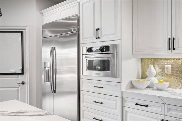 kitchen featuring stainless steel appliances, light stone countertops, white cabinets, and decorative backsplash