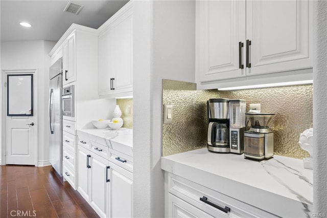 kitchen featuring white cabinetry, dark hardwood / wood-style flooring, light stone countertops, and decorative backsplash