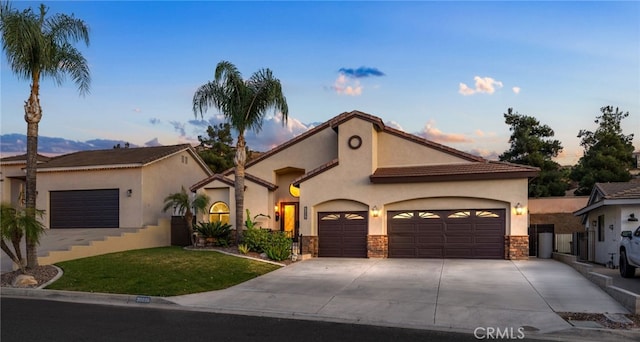 mediterranean / spanish home with stucco siding, concrete driveway, an attached garage, stone siding, and a front lawn