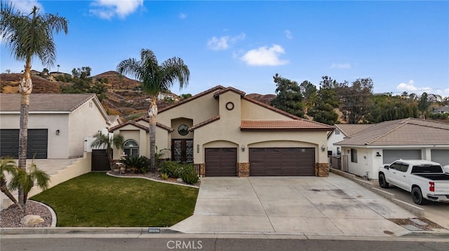 mediterranean / spanish house featuring a front lawn, driveway, an attached garage, and stucco siding