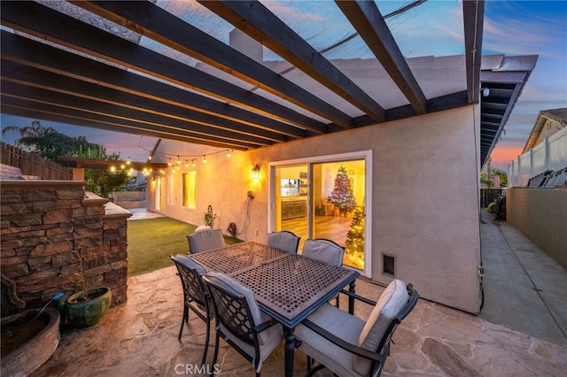 patio terrace at dusk featuring fence, outdoor dining area, and a pergola