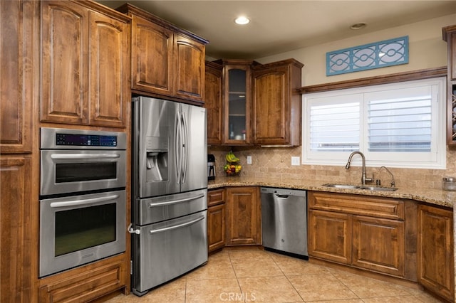 kitchen with light tile patterned floors, backsplash, appliances with stainless steel finishes, a sink, and light stone countertops