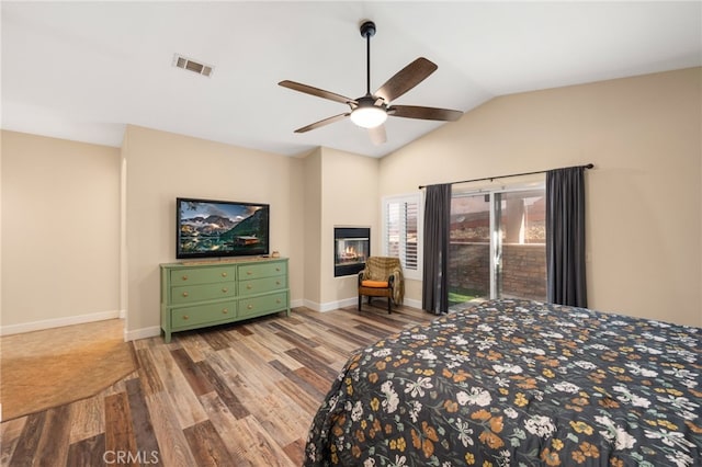 bedroom featuring visible vents, a glass covered fireplace, vaulted ceiling, wood finished floors, and baseboards