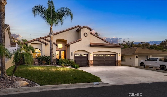 mediterranean / spanish-style home featuring stucco siding, a front yard, a garage, stone siding, and driveway