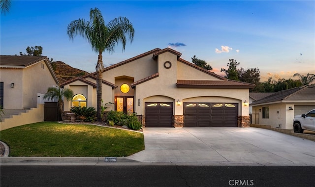 mediterranean / spanish house featuring an attached garage, concrete driveway, a yard, a tiled roof, and stucco siding