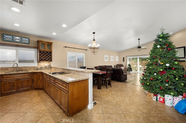 kitchen with brown cabinets, a peninsula, light stone countertops, a sink, and light tile patterned flooring