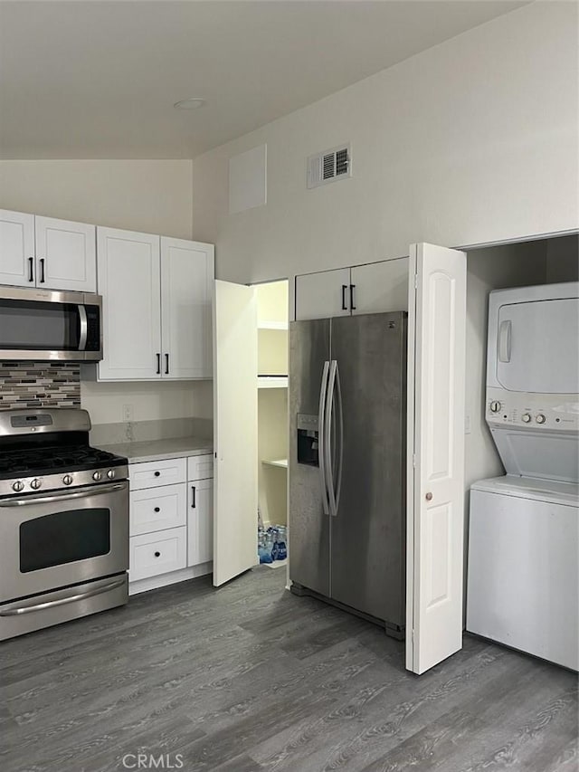 kitchen with stainless steel appliances, stacked washer and clothes dryer, dark hardwood / wood-style flooring, and white cabinetry