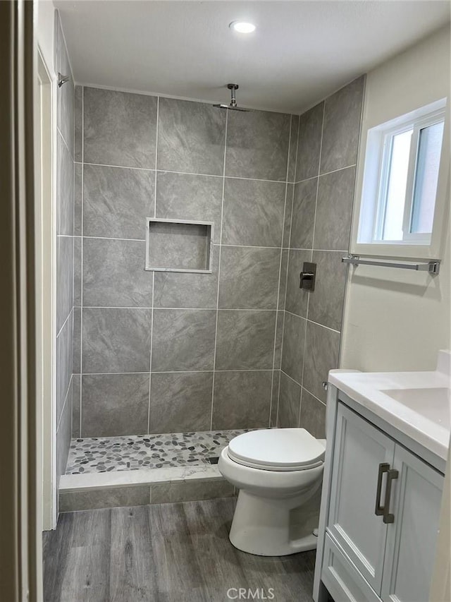 bathroom featuring toilet, a tile shower, wood-type flooring, and vanity