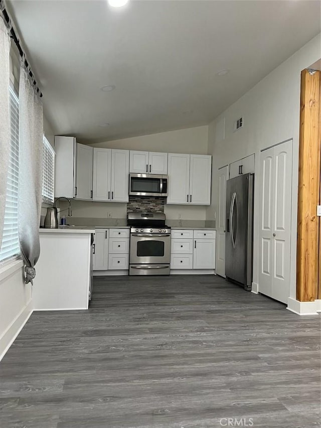 kitchen featuring appliances with stainless steel finishes, white cabinetry, dark hardwood / wood-style flooring, tasteful backsplash, and vaulted ceiling