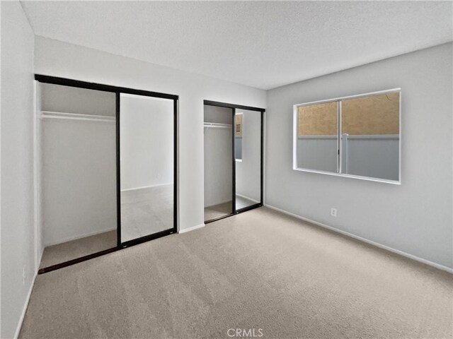 unfurnished bedroom featuring light colored carpet, a textured ceiling, and multiple closets