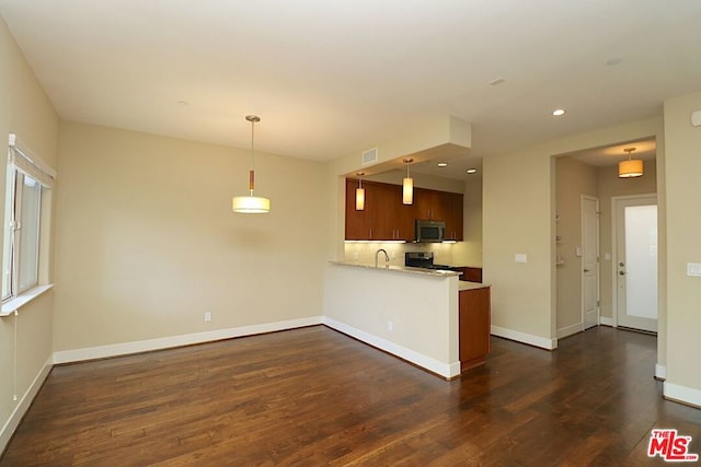 kitchen with dark wood-type flooring, appliances with stainless steel finishes, pendant lighting, and kitchen peninsula