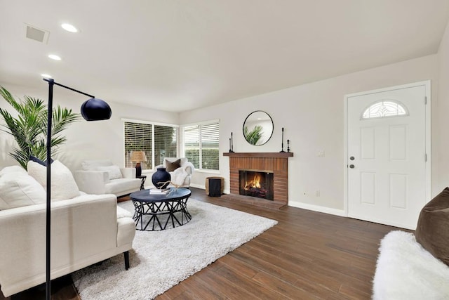 living room with a brick fireplace and dark hardwood / wood-style flooring