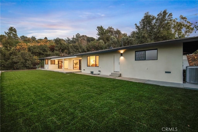 back house at dusk featuring a lawn, central AC, and a patio area