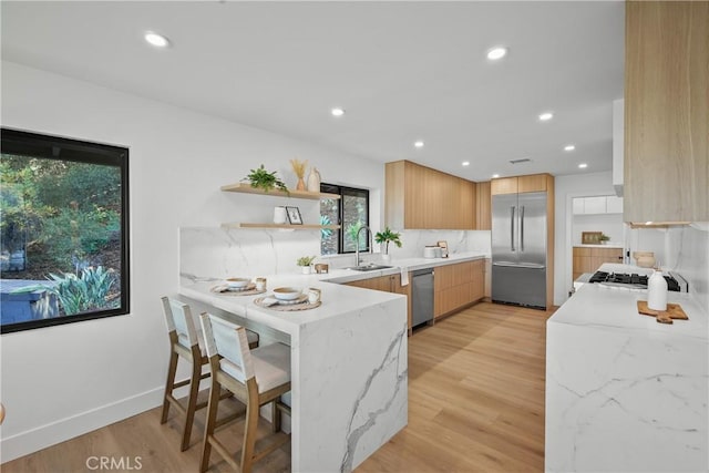 kitchen featuring a breakfast bar, light brown cabinetry, light hardwood / wood-style flooring, appliances with stainless steel finishes, and kitchen peninsula