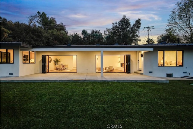 back house at dusk featuring a patio and a yard