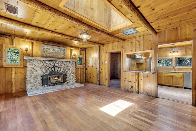 unfurnished living room with wooden ceiling, beamed ceiling, a wood stove, light hardwood / wood-style flooring, and sink