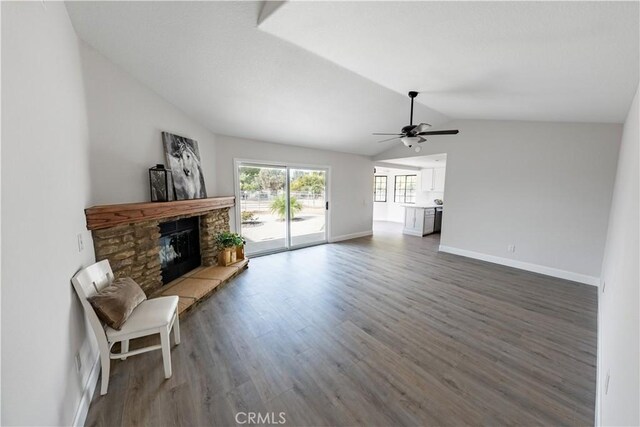 living room featuring ceiling fan, dark wood-type flooring, a stone fireplace, and vaulted ceiling