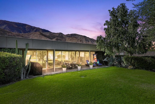 back house at dusk featuring a mountain view, a lawn, and a patio