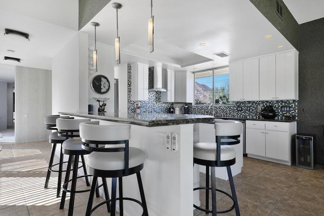 kitchen with a breakfast bar area, wall chimney exhaust hood, white cabinetry, and pendant lighting