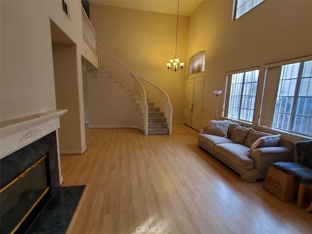 living room featuring a high ceiling, wood-type flooring, a premium fireplace, and a notable chandelier