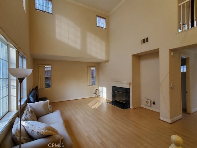 living room featuring a high end fireplace, ornamental molding, a towering ceiling, and light hardwood / wood-style flooring