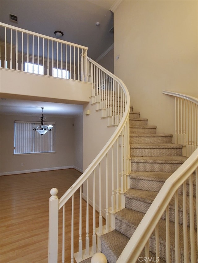 stairs with hardwood / wood-style flooring, ornamental molding, and an inviting chandelier