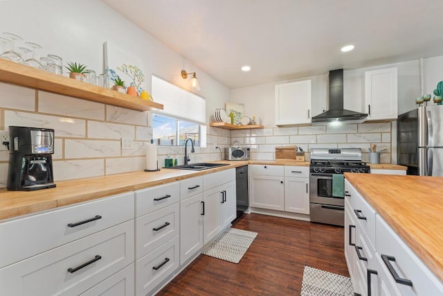 kitchen with wooden counters, white cabinetry, wall chimney range hood, stainless steel appliances, and sink