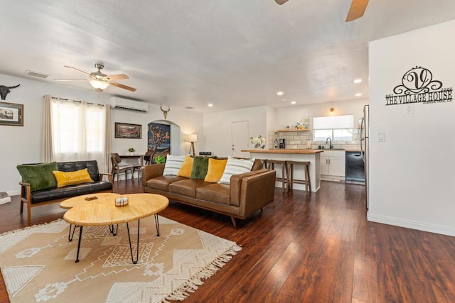 living room featuring a wall unit AC, ceiling fan, a healthy amount of sunlight, and dark hardwood / wood-style floors