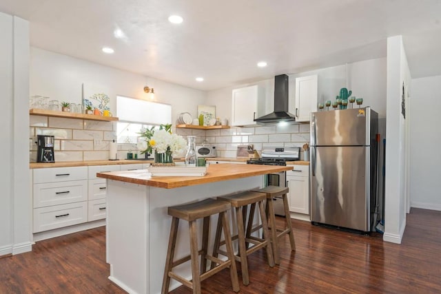 kitchen featuring white cabinets, wall chimney exhaust hood, a kitchen island, butcher block counters, and stainless steel appliances