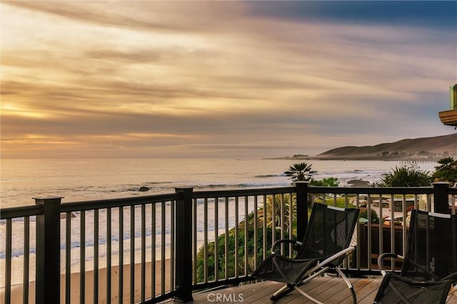 balcony at dusk featuring a water view and a beach view