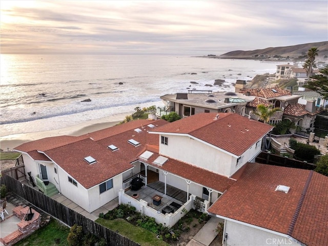 aerial view at dusk featuring a water view and a beach view