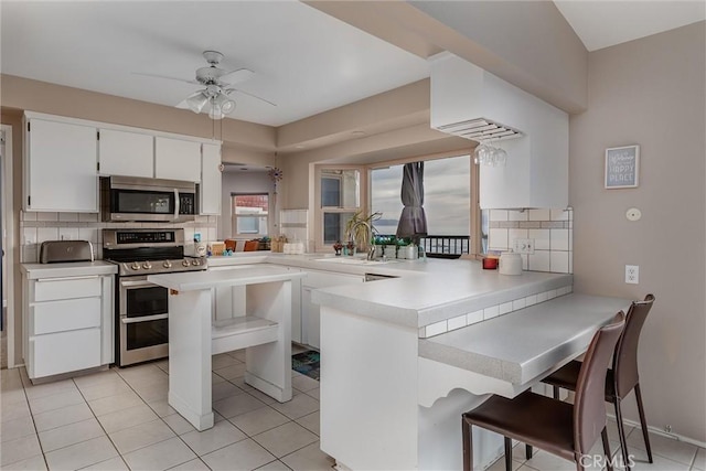 kitchen featuring white cabinetry, appliances with stainless steel finishes, kitchen peninsula, and a breakfast bar area