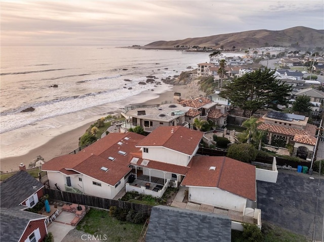 aerial view at dusk featuring a water and mountain view and a view of the beach