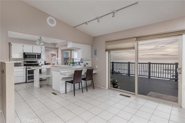 kitchen featuring ceiling fan, vaulted ceiling, decorative backsplash, stainless steel appliances, and white cabinets