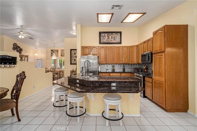 kitchen with decorative backsplash, light tile patterned flooring, a kitchen island with sink, a breakfast bar area, and stainless steel appliances