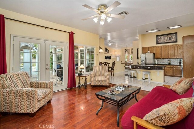 living room with light wood-type flooring, french doors, sink, and ceiling fan