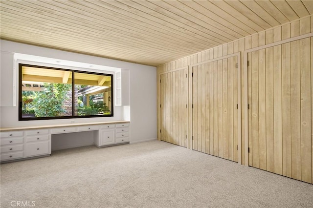 carpeted empty room with built in desk, wooden ceiling, and wood walls