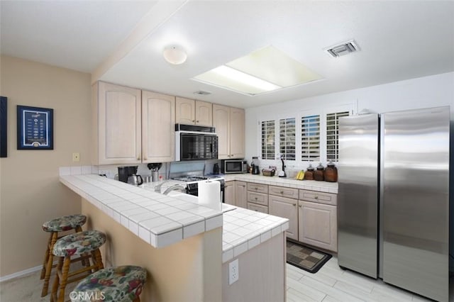 kitchen featuring black appliances, kitchen peninsula, tile countertops, and a breakfast bar area